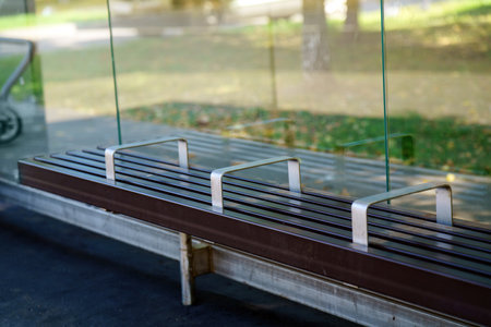 bus stop bench features metal ridges designed to deter sleeping, highlighting societal attitudes towards homelessness public space usage. It reflects a complex relationship between comfort and exclusionの写真素材