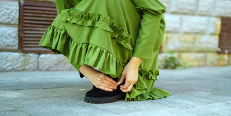 woman in a flowing green dress delicately fastens the strap of her elegant shoe, embodying grace and poise. This moment captures the essence of beauty in simplicityの写真素材