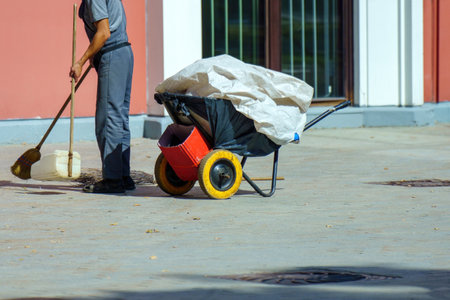 street cleaner in uniform, diligently sweeping trash into a makeshift scoop beside a cart. It highlights the importance of cleanliness and the dedication of those who maintain our environmentの写真素材