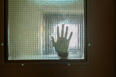 hand pressed against a grid-patterned glass symbolizes the intersection of human connection and...
