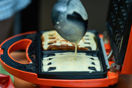 vibrant plastic ladle gracefully pours smooth batter into a sleek electric waffle maker, poised to...