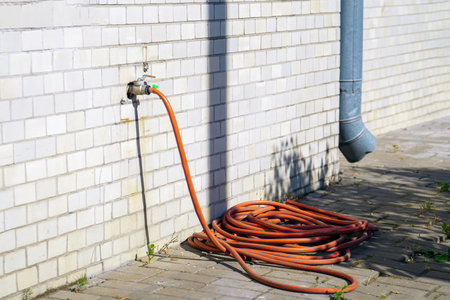 orange garden hose stretches from a faucet protruding from a white brick wall, symbolizing the connection between man-made structures and nature. It embodies utility and harmony in designの写真素材
