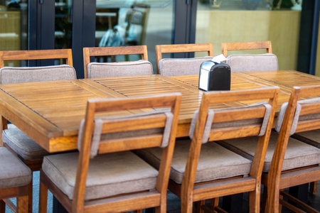cozy outdoor cafe setting, rustic wooden chairs encircle a long table, inviting guests to share stories and laughter. Sunlight filters through trees, creating a warm and welcoming ambianceの写真素材