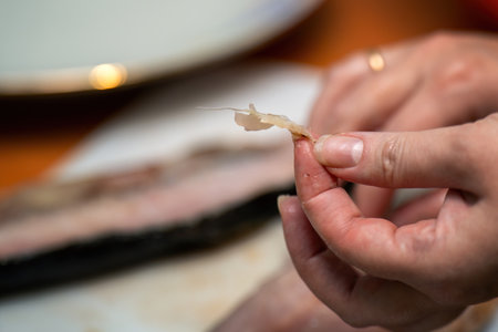 fingers holding a bone extracted from raw red fish during cleaning. This moment highlights the transition from nature to culinary preparation, emphasizing the connection between food and craftsmanshipの写真素材