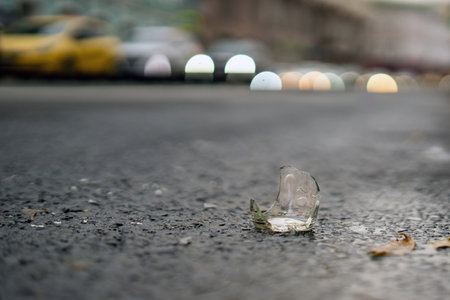 broken glass bottle with sharp edges rests on a paved road, a stark reminder of negligence. Its transparent shards glimmer dangerously, posing risks to passing vehicles and pedestrians alikeの写真素材