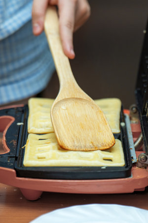 bamboo spatula pressing waffles in an electric waffle maker, illustrating the blend of natural materials and modern kitchen convenience, highlighting culinary creativity and home cooking joyの写真素材