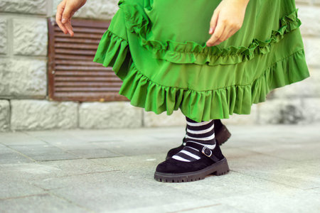 girl in a green dress and striped knee-highs crouches down to tie her shoes, showcasing innocence and playful spirit. The moment captures childhood charm and vibrant fashionの写真素材