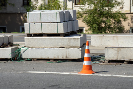 road under repair, featuring granite rectangular blocks placed alongside a warning cone, signifies...