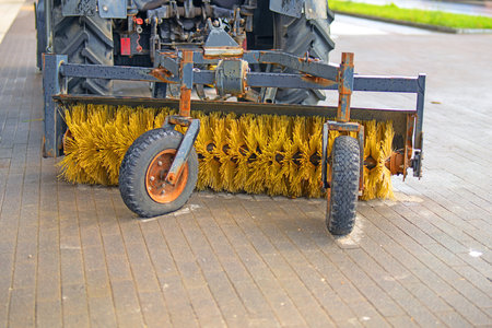 cylindrical plastic broom designed for sweeping roads and sidewalks, positioned behind a tractor,...