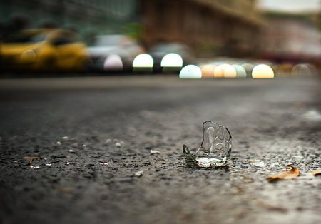 broken glass bottle with sharp edges rests on a paved road, a stark reminder of negligence. Its...