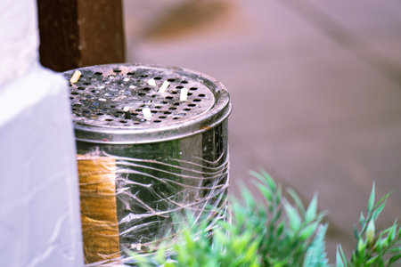 cylindrical metal trash bin topped with a grid-shaped ashtray filled with cigarette butts, representing discarded habits and urban waste managementの写真素材
