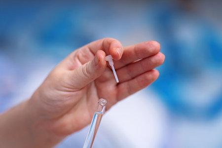 hand holding a plastic stick attached to a cap, removed from a glass vial containing a transparent medication. Ideal for healthcare, pharmaceutical, and medical imagingの写真素材