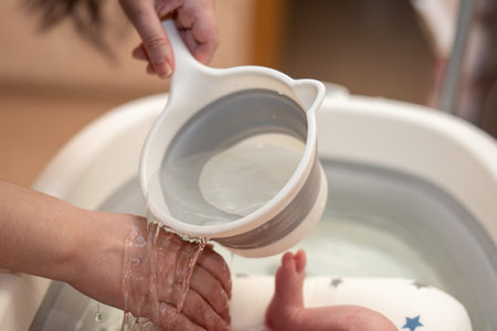 woman's hand gently pours water onto the outer side of her palm to test the temperature for bathing a child in a bathtub, ensuring a safe and comfortable experienceの写真素材