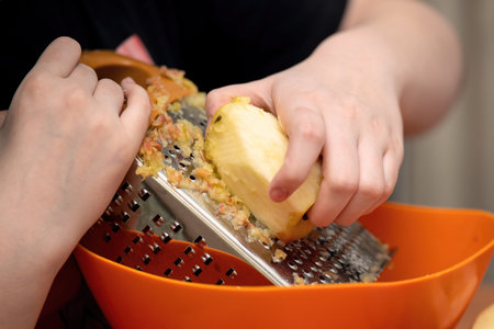 fresh apples being grated on a fine metal grater, perfect for pie filling. The vibrant red apple...