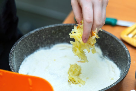hand pouring gratified apples into a raw pie for filling, showcasing the preparation of a delicious homemade dessertの写真素材