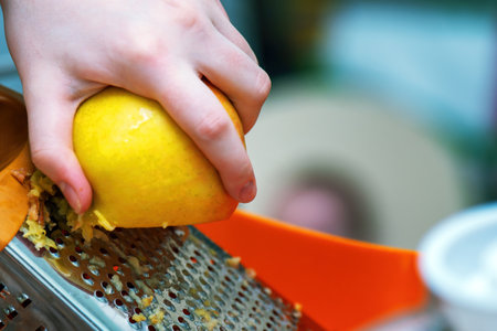 fresh apples being grated on a fine metal grater, perfect for pie filling. The vibrant red apple skins contrast with the metallic grater, showcasing kitchen preparationの写真素材