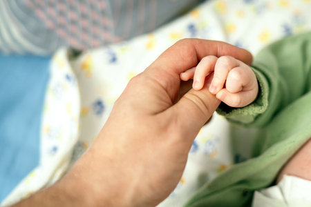 A fathers hand tenderly holds his newborn babys tiny hand, symbolizing love, protection, and the precious bond between parent and childの写真素材