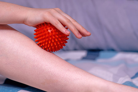 A woman performs self-massage on her feet using a red spiky rubber ball.の写真素材