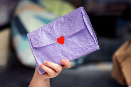 woman's hand holds a purple kraft paper love letter sealed with a red heart sticker, symbolizing romance and heartfelt emotionsの写真素材
