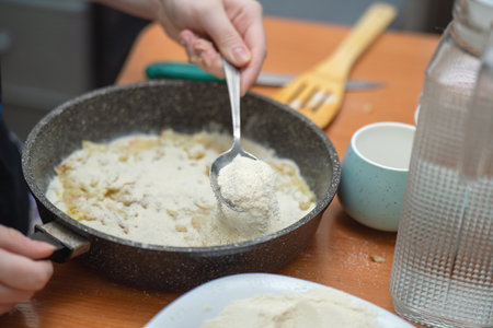 metal spoon sprinkles sugar over a raw apple pie, capturing the sweet preparation of a rustic homemade dessertの写真素材