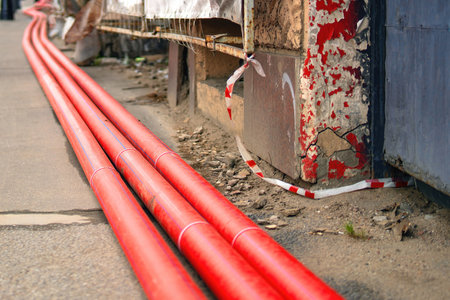 Three large red plastic sewer pipes installed near a building under renovation, showcasing urban infrastructure work.の写真素材