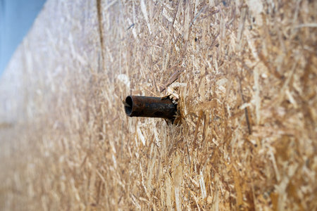 Metal pipe penetrating through a chipboard (DSP) plane, showing industrial force or accidental...