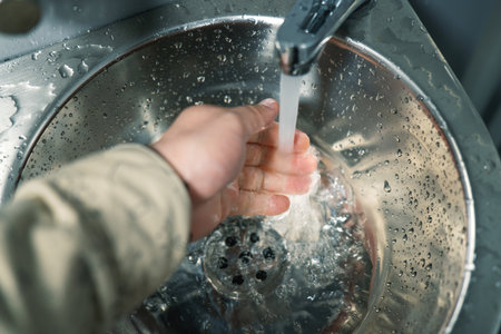 Person washing hands at a clean stainless steel public sink, showcasing hygiene maintenance in shared spacesの写真素材
