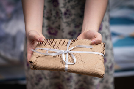 Young woman offering a gift-wrapped book in craft perforated paper with a bow, showing casing...