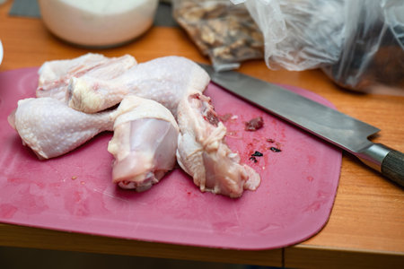 Chopped chicken drumsticks on a plastic cutting board with a knife nearby, ready for cooking preparation.の写真素材