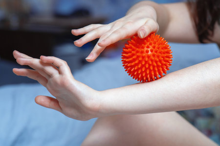 Young woman self-massaging her feet with a red spiky rubber ball for relaxation and muscle relief.の写真素材
