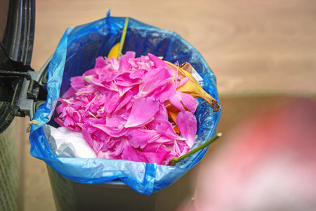 Trash bin filled with fresh pink peony petals, creating a striking contrast between waste and natural beauty.の写真素材