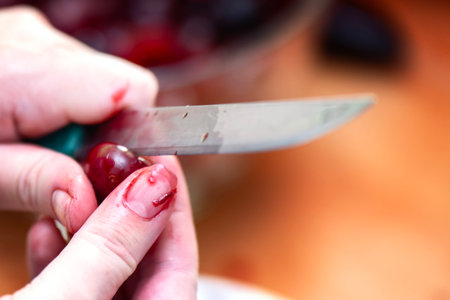 Woman's fingernail stained with red cherry juice as hands chop fresh berries, showing messy cooking...
