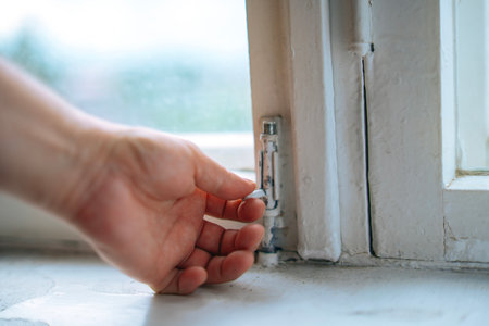 Male hand opening a vintage latch on an old wooden-framed window, showcasing rustic charm and...