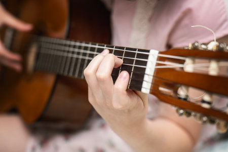 Child's hand learning to play guitar, forming chords on the fretboard during a lesson.