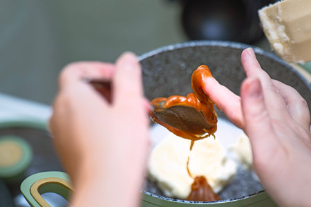 Female hand scraping natural honey from a metal spoon for dessert preparation.の写真素材