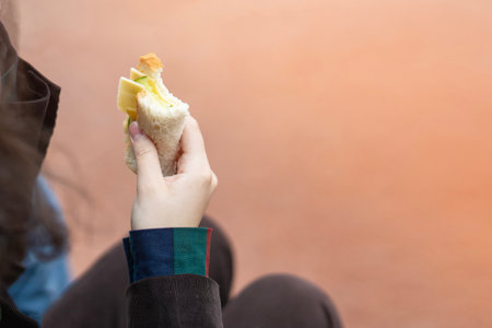 Teen's hand holding a homemade sandwich with toast bread, cheese, and cucumber.の写真素材