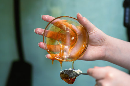 A girl's hand scraping fresh honey from a transparent glass bowl held in hand.の写真素材