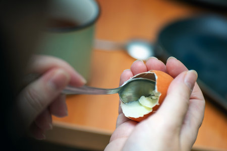 Metal teaspoon scooping the last remnants of boiled egg from its shell.