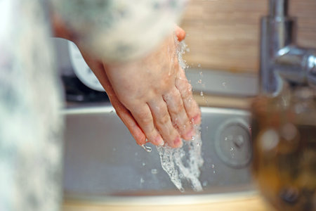Teenager washing hands under running water at home. Basic hygiene routine.