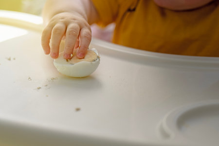 A small child's hand reaching for a boiled egg half at a kids table during weaning to solid foods.の写真素材