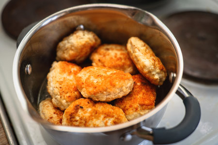 Multiple fried chicken patties stacked in a metal pot for keeping warm and steaming.
