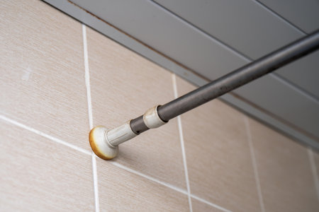 End of an old shower curtain rod pressed against tiled bathroom wall.の写真素材