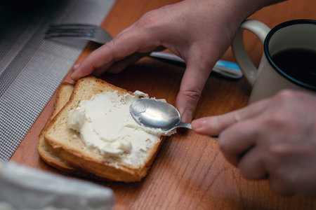 Spreading cottage cheese on crispy toast with a metal teaspoon for breakfast.