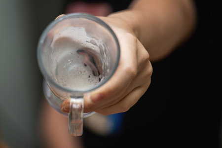 Teenager's hand holding an empty glass, showing only a few leftover milk droplets inside. glass,...