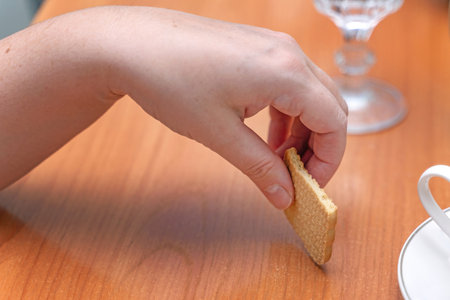 A woman's hand holding half of a rectangular biscuit during a tea time break.の写真素材