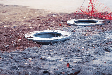 Open construction manholes next to a pedestrian path with damaged orange safety fencing.の写真素材