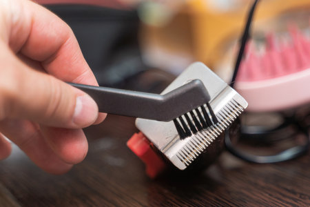 Cleaning hair clippers with a small brush, removing cut hairs from the blades for maintenance.
