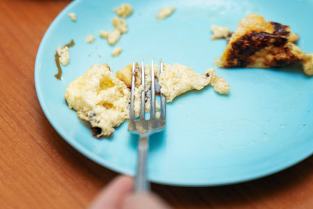 Metal fork crushing a fluffy omelette on a plate during a home breakfast.の写真素材