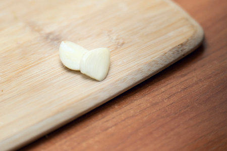Freshly peeled garlic clove halves on a bamboo cutting board over a wooden table.の写真素材