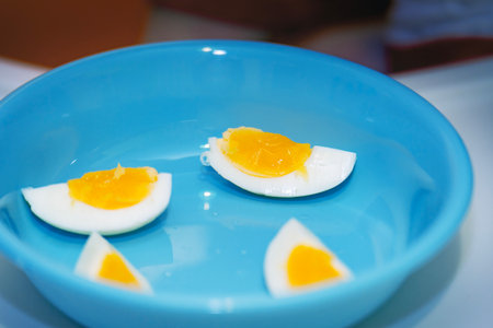 Soft-boiled egg, quartered vertically, served on a blue plastic plate for a child.の写真素材